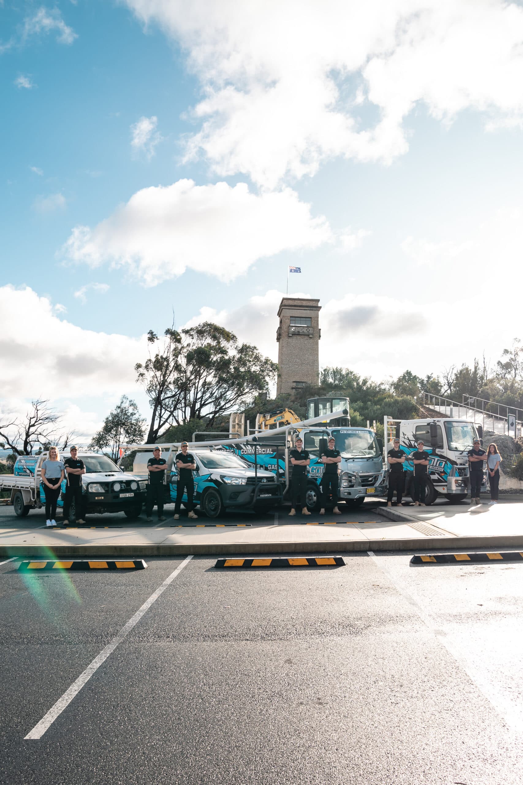 Team of workers standing with company vehicles and equipment outdoors.